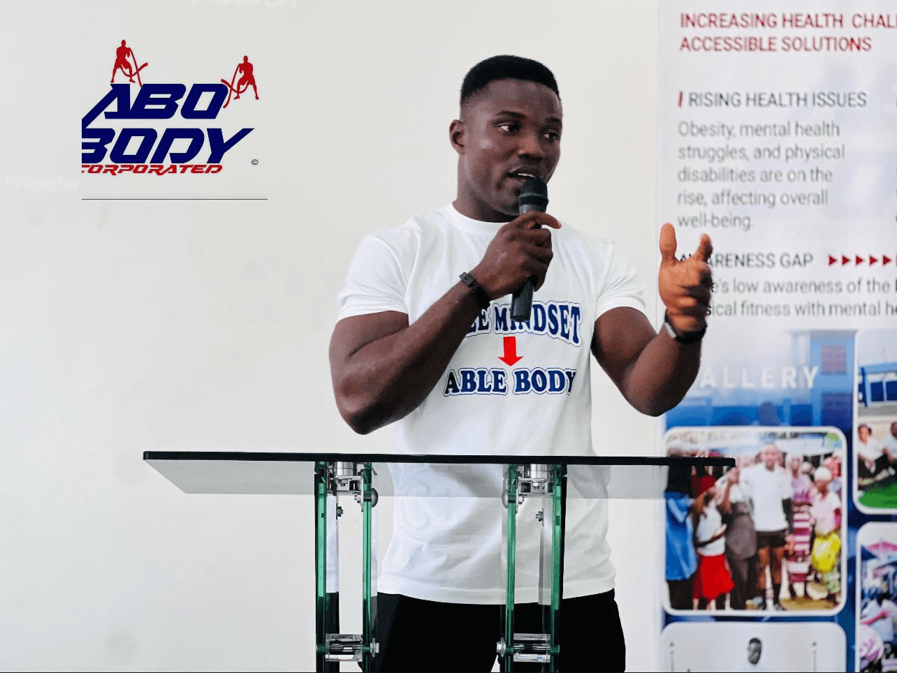 Abel Gebor speaking, wearing an ABO BODY 'Able Mindset, Able Body' shirt